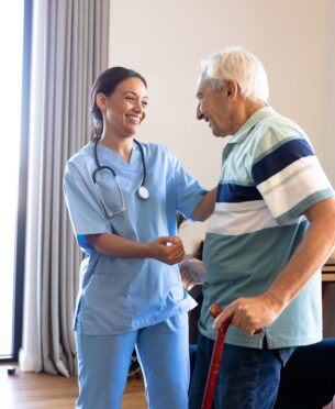 Biracial female physiotherapist assisting caucasian senior man in standing with walking cane at home. Copy space, unaltered, physical therapy, healthcare, retirement, recovery, support, disability.