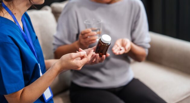 Caucasian female doctor provides a glass of water and medication pills to an elderly Asian